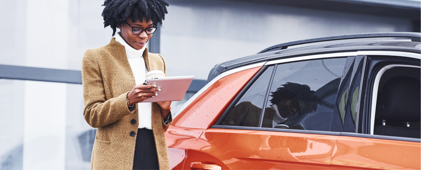 A entrepreneur managing her carsharing business in her mobile device, standing next to her car.